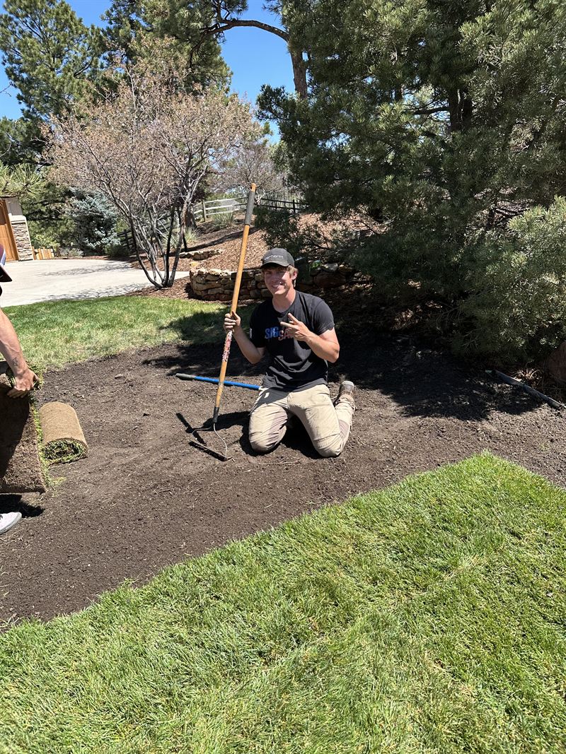 Mason kneeling on freshly graded soil during a sod install, rake in hand