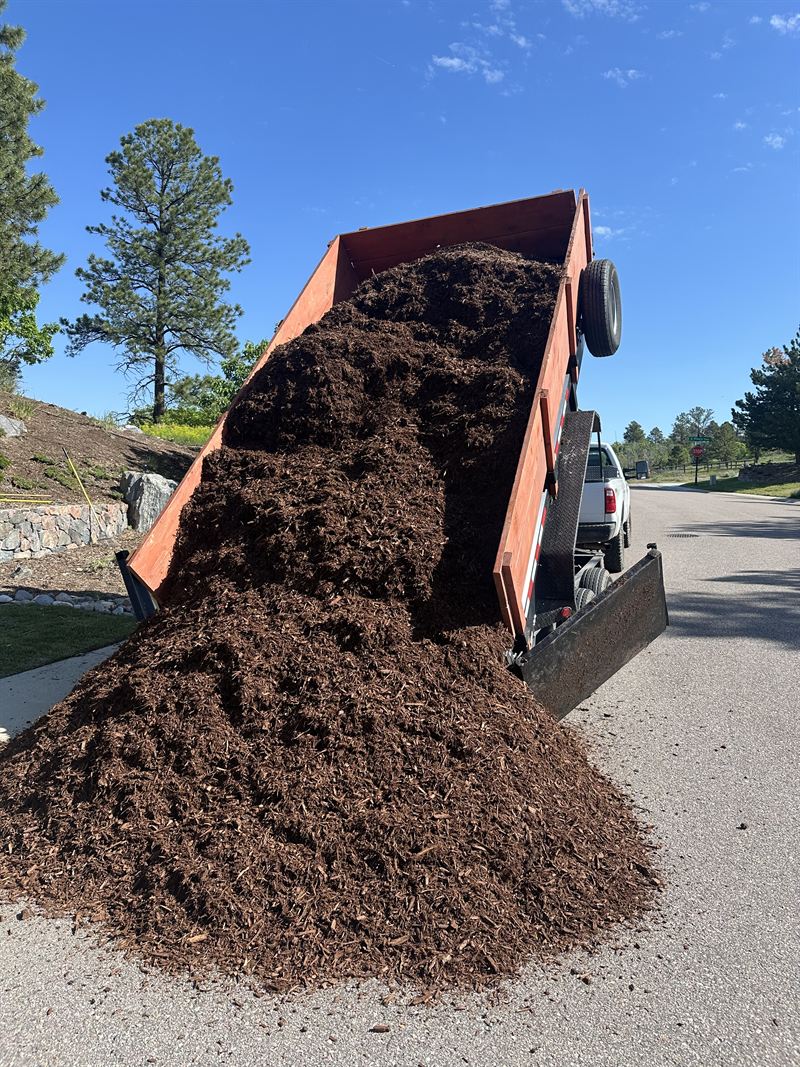 A dump trailer tipping a load of mulch onto the street at a job site