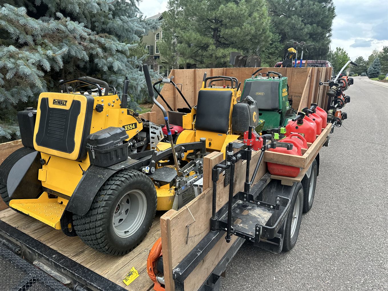 A trailer packed with stand-on mowers, a reel mower, trimmers, and fuel cans